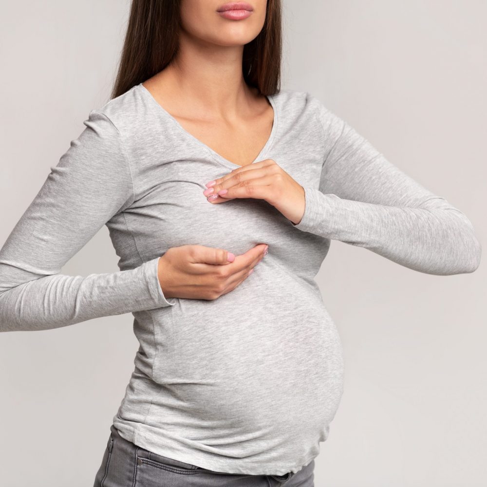 Sore Breasts. Unrecognizable Pregnant Lady Suffering From Pain Touching Chest Standing Over Gray Studio Background. Cropped
